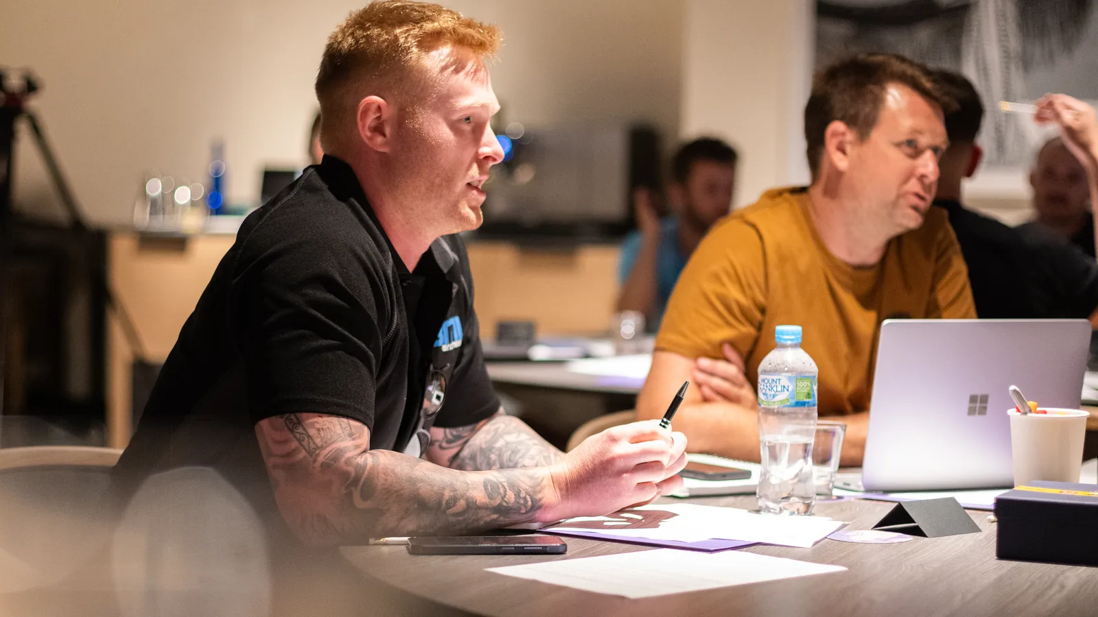 Two trade business owners in mid-conversation across a table, a laptop open between them