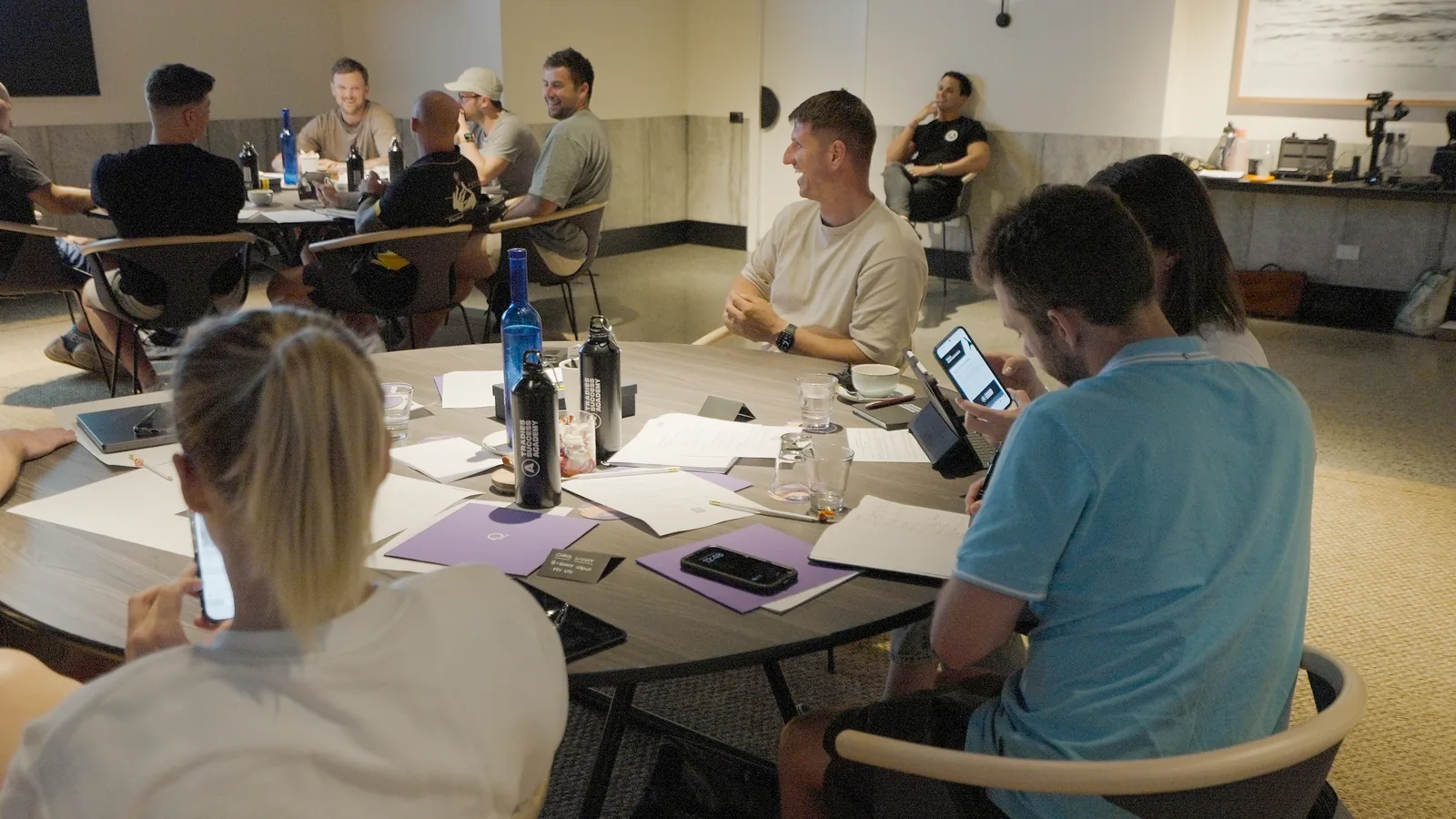 Trade business owners at round tables in an Academy session, worksheets and laptops out, building their own systems