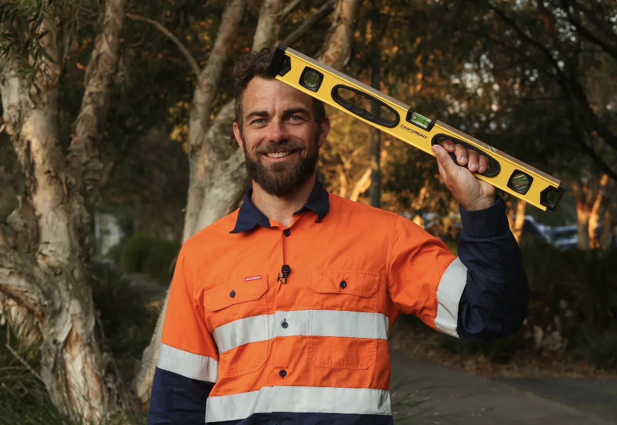 Greg Allan in high-visibility workwear holding a level